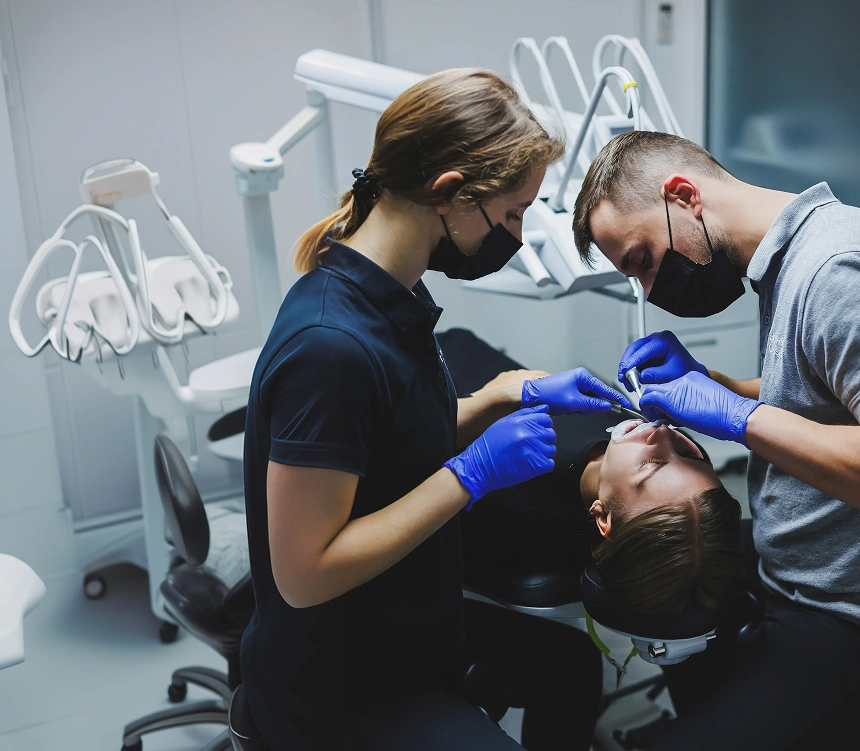 Two dental professionals performing an oral surgery procedure on a patient in a modern dental treatment room.